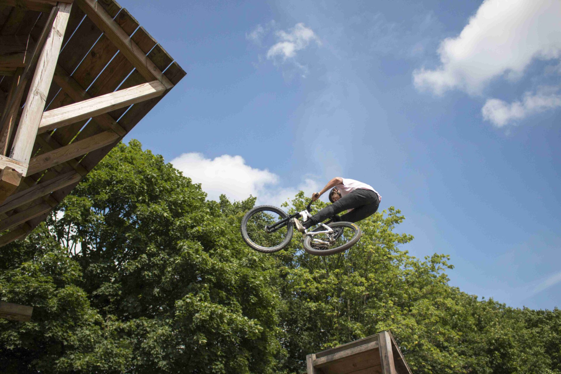 Ein Mountainbiker springt mit seinem Fahrrad in die Luft über eine Rampe im Bikepark unter blauem Himmel.