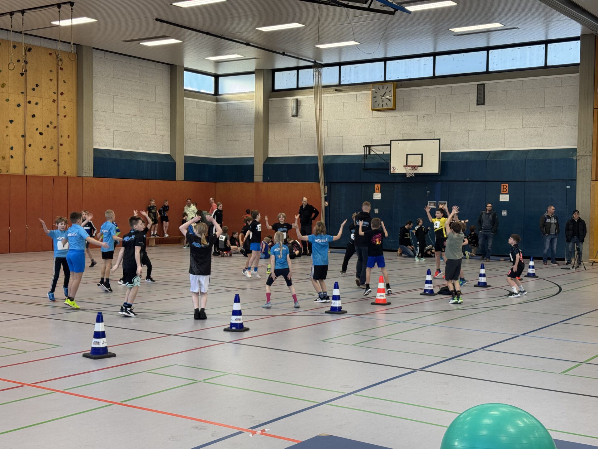 Kinder machen in einer Sporthalle Hampelmänner.