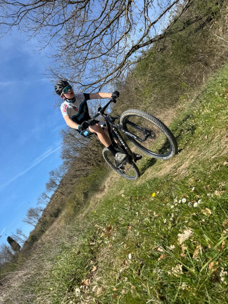 Ein junger Mountainbiker fährt mit Schwung durch die grüne Landschaft während des Trainingslagers in der Toskana.