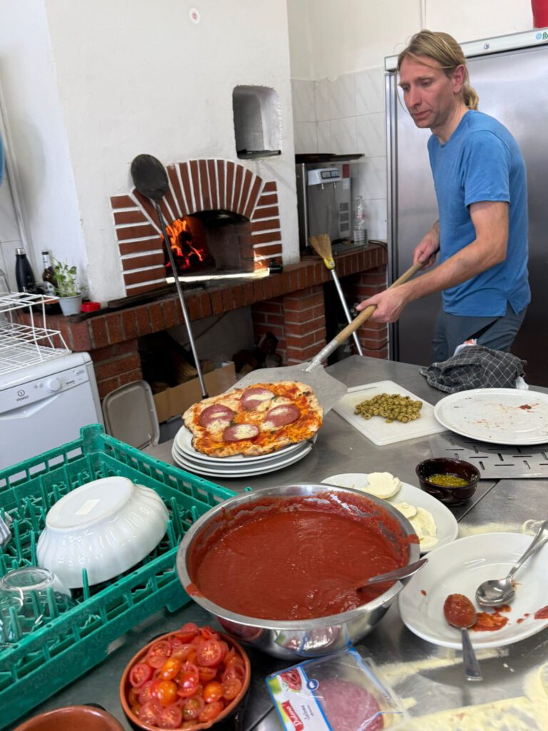 Ein Koch bereitet frisch gebackene Pizza in der Küche während des Trainingslagers in der Toskana vor.