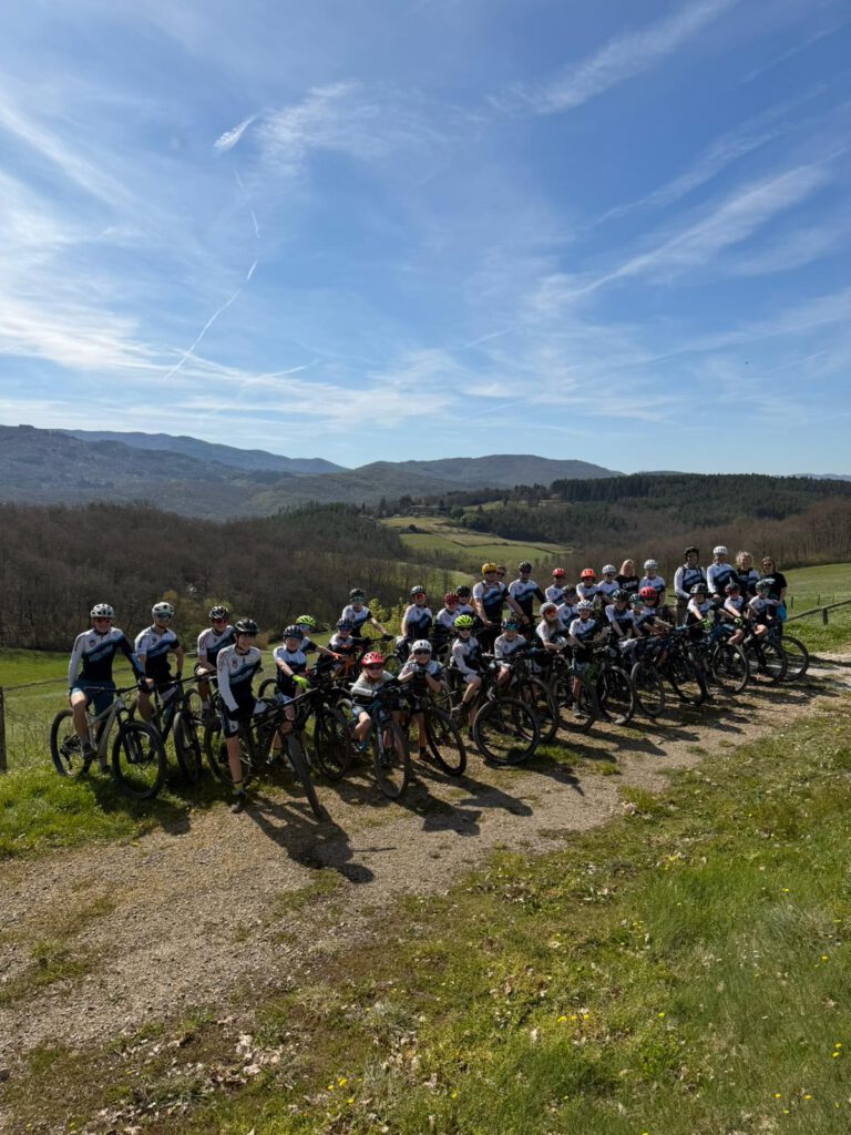 Die Teilnehmer des Trainingslagers in der Toskana posieren lächelnd auf ihren Mountainbikes vor einer malerischen Landschaft.