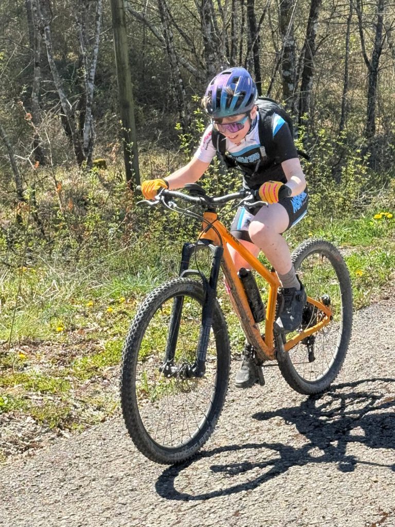 Ein junger Radfahrer mit Sonnenbrille und Handschuhen fährt mit einem orangefarbenen Mountainbike durch die Toskana.